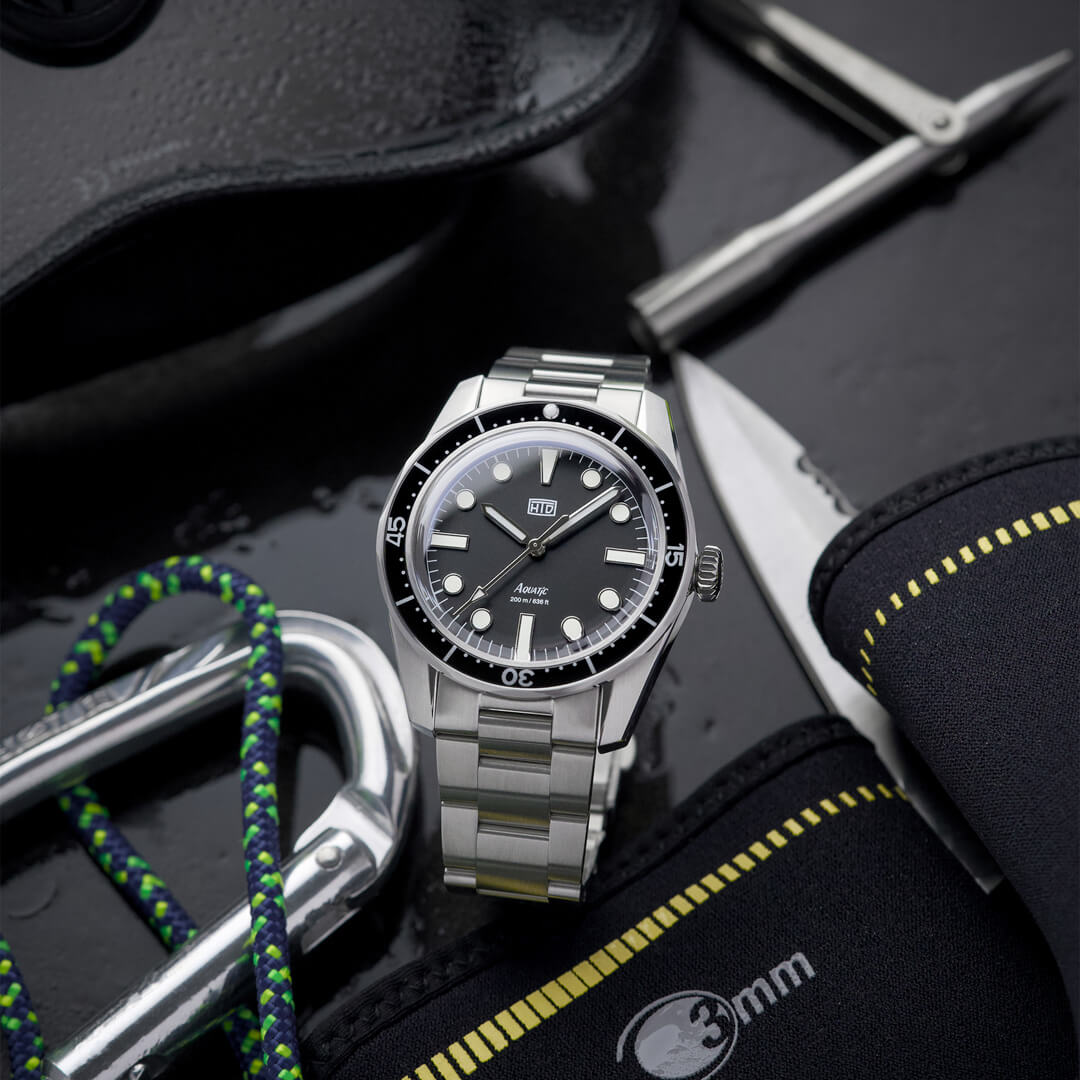 Orologio HTD Aquatic diver in acciaio con quadrante nero, posato tra attrezzatura subacquea con corda, coltello e muta.