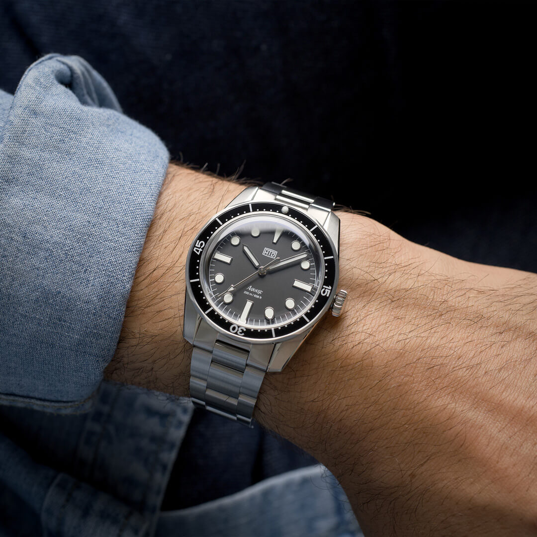 Orologio HTD Aquatic diver in acciaio al polso, con quadrante nero e ghiera nera, indossato con camicia di jeans.