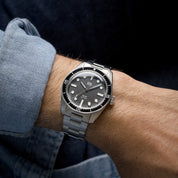 Orologio HTD Aquatic diver in acciaio al polso, con quadrante nero e ghiera nera, indossato con camicia di jeans.