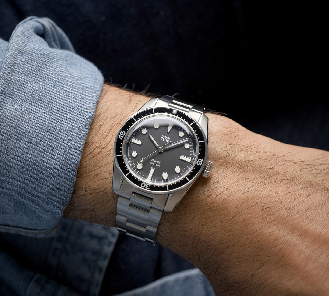 Orologio HTD Aquatic diver in acciaio al polso, con quadrante nero e ghiera nera, indossato con camicia di jeans.