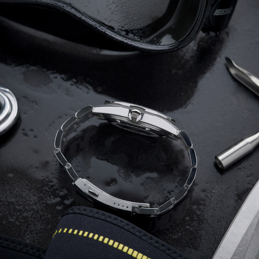 Vista laterale del bracciale e della chiusura logata HTD dell’orologio Aquatic Spaceboy, appoggiato su superficie bagnata con attrezzatura da immersione.