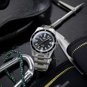 Orologio diver HTD Aquatic Spaceboy con quadrante nero e ghiera nera, posato tra accessori subacquei come moschettone, muta e coltello.