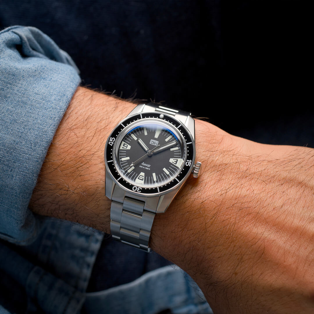 Orologio HTD Aquatic Spaceboy al polso, con quadrante nero e ghiera girevole, indossato con camicia di jeans.