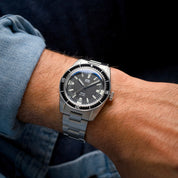 Orologio HTD Aquatic Spaceboy al polso, con quadrante nero e ghiera girevole, indossato con camicia di jeans.