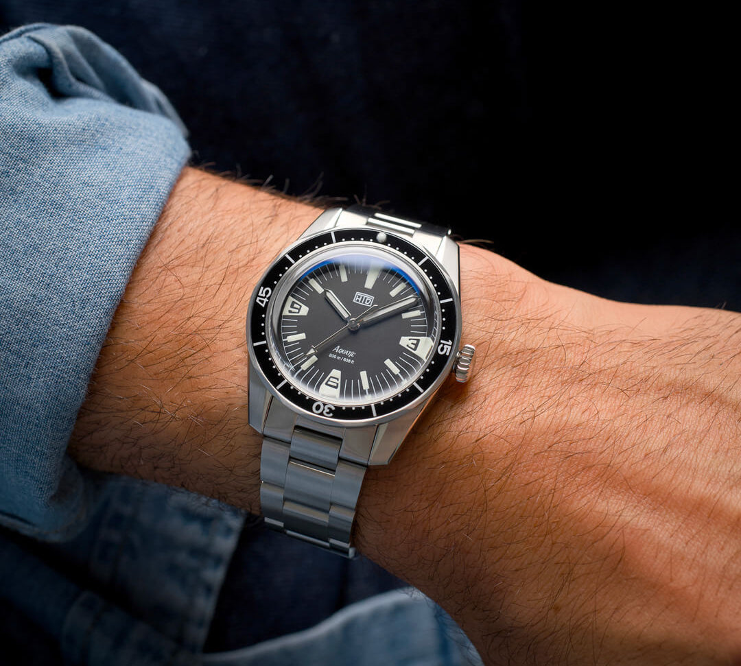 Orologio HTD Aquatic Spaceboy al polso, con quadrante nero e ghiera girevole, indossato con camicia di jeans.