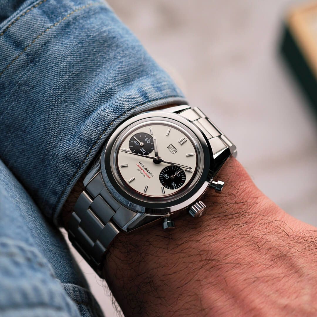 Orologio cronografo in acciaio con quadrante panna e contatori neri, indossato al polso con camicia di jeans.