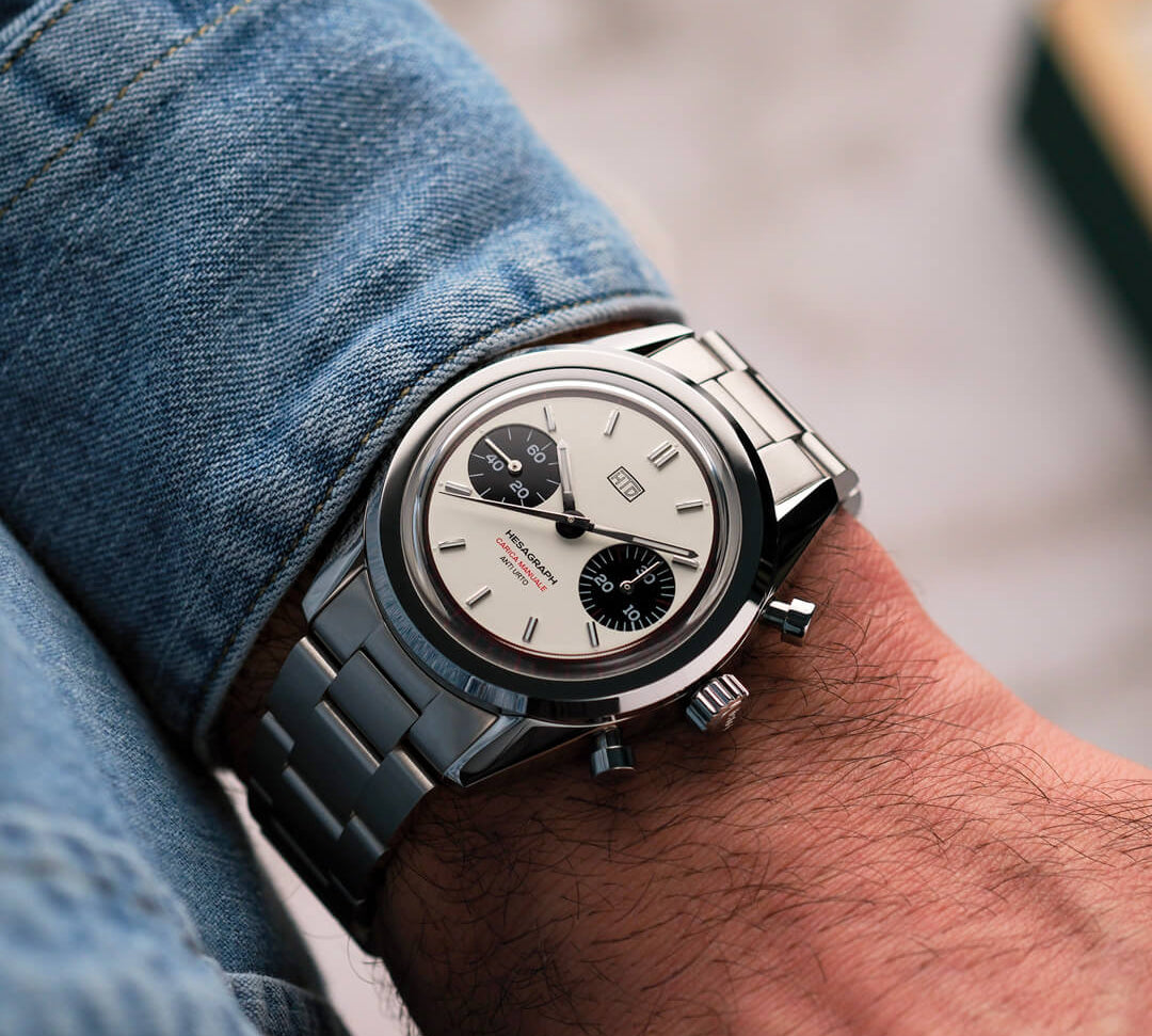 Orologio cronografo in acciaio con quadrante panna e contatori neri, indossato al polso con camicia di jeans.