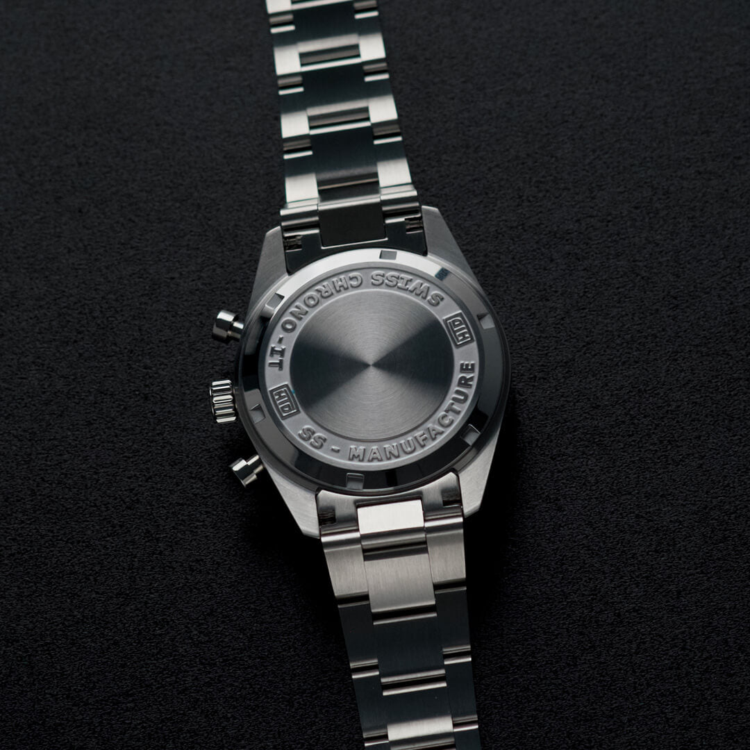 Fondello in acciaio di un orologio cronografo con incisioni e bracciale metallico, su sfondo nero.