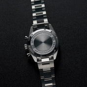 Fondello in acciaio di un orologio cronografo con incisioni e bracciale metallico, su sfondo nero.