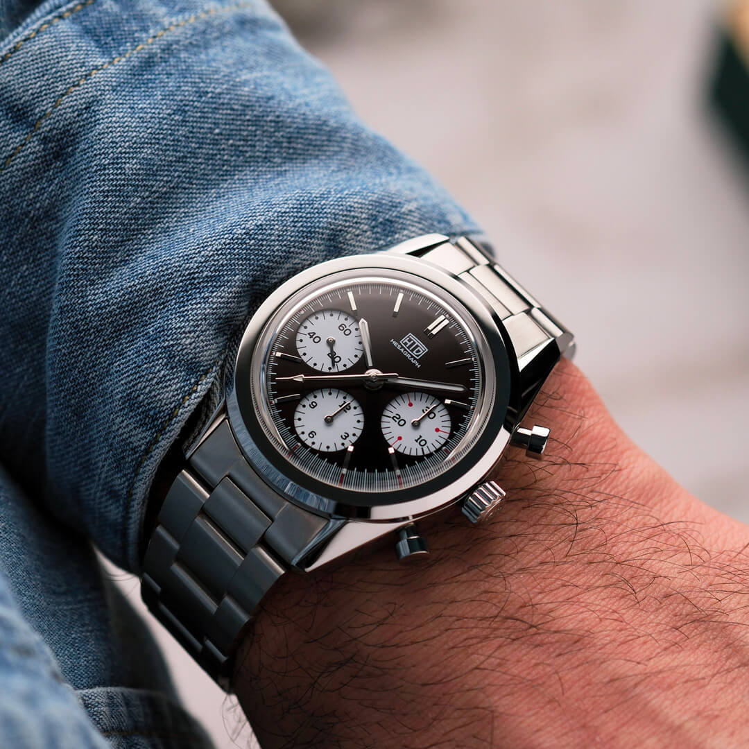 Orologio cronografo da polso in acciaio con quadrante nero e contatori bianchi, indossato con camicia di jeans.