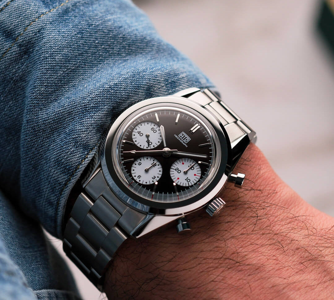 Orologio cronografo da polso in acciaio con quadrante nero e contatori bianchi, indossato con camicia di jeans.