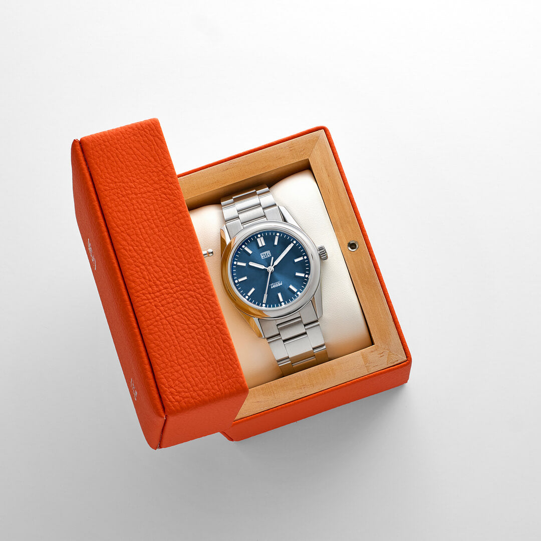 Orologio HTD Tennis Chic nella sua scatola arancione, con quadrante blu acceso e bracciale in acciaio.
