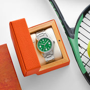 Orologio HTD Tennis Erba con quadrante verde presentato all’interno della scatola arancione, accanto a racchetta e pallina da tennis.