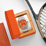 Orologio HTD Tennis Terra con quadrante arancione in esposizione all’interno della scatola arancione, accanto a una racchetta da tennis.
