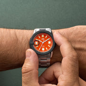 Orologio HTD Tennis Terra con quadrante arancione indossato al polso, protetto da un copri-quadrante nero in gomma.